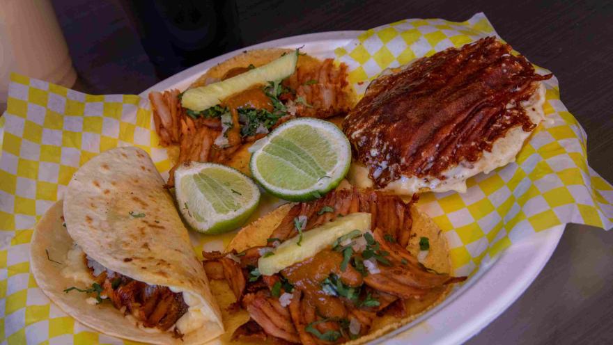 Plato con tacos al pastor, quesadilla, limón, pepino y salsas.