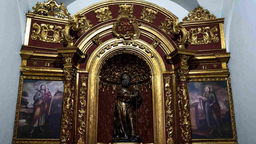 Retablo dorado de la Iglesia de San Juan de Dios, con una imagen central de un santo y pinturas religiosas enmarcadas en una ornamentada estructura barroca.