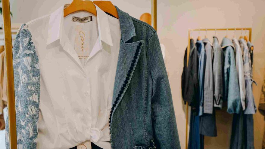 Prendas de diseño colombiano exhibidas en una tienda de moda, con camisas, chaquetas y otras piezas de vestir en tonos neutros y azules.