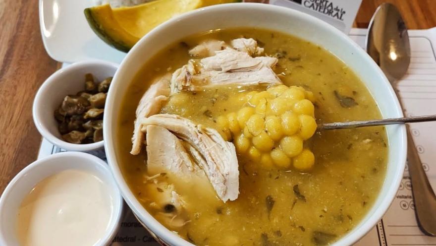 Ajiaco santafereño servido con pollo, mazorca y papa, acompañado de aguacate y alcaparras.