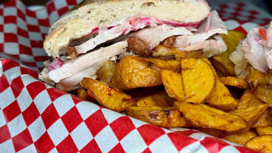 Sánduche de chicharrón con cebolla encurtida y papas doradas.