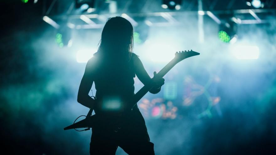 Silueta de guitarrista en concierto, iluminado por luces intensas y humo en el escenario durante una presentación en vivo.