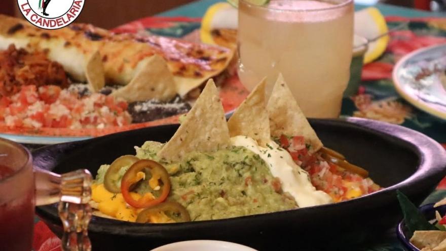 Nachos with guacamole, sour cream, cheese, pico de gallo, and jalapeños, accompanied by enchiladas and a beverage.