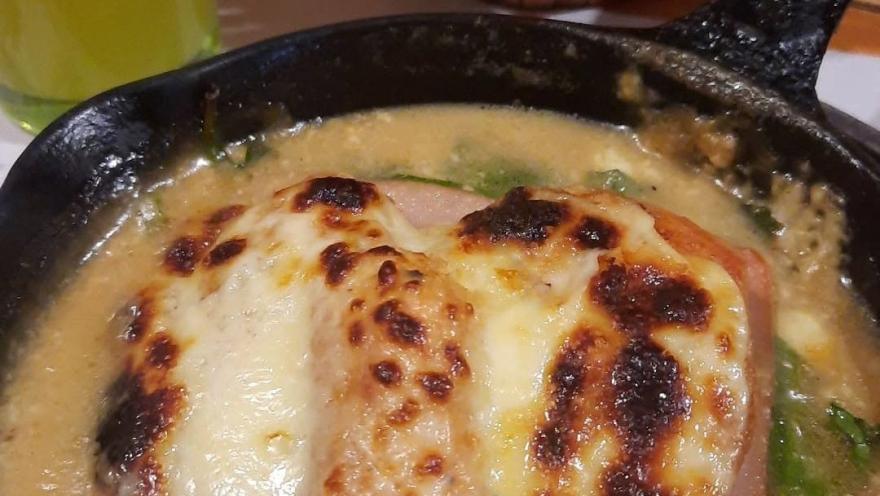 Pollo gratinado con queso, servido en salsa cremosa en una sartén de hierro.