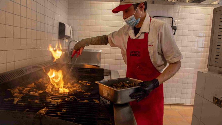 Cocinero preparando carne a la parrilla en la cocina de Los Tacos Norteños.