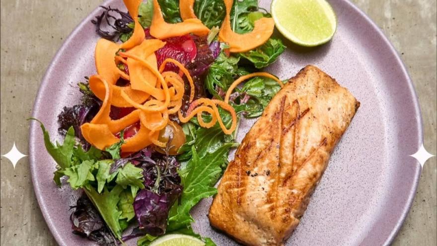 Filete de pescado a la parrilla acompañado de ensalada de hojas verdes, zanahoria en láminas, remolacha y rodajas de limón.