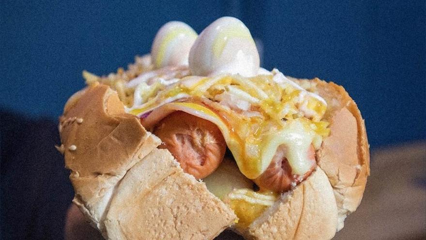 Perro caliente con salchicha, queso, salsas y toppings variados.