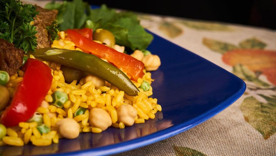 Plato de arroz con garbanzos, arvejas y pimentones, acompañado de vegetales frescos y una porción de proteína vegetal.