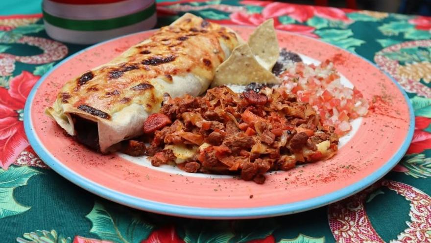 A plate of tacos with meat, chorizo, beans, pico de gallo, and totopos, accompanied by a cheese-topped, baked burrito.
