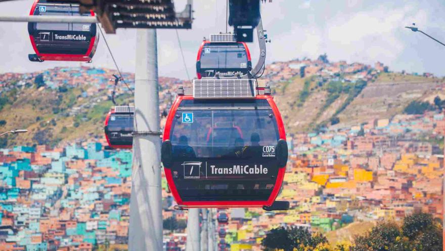 Cabinas del TransMiCable recorriendo Ciudad Bolívar, con el paisaje urbano y las coloridas viviendas de la localidad al fondo.