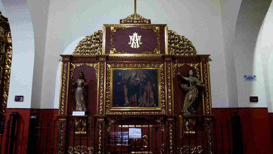 Retablo religioso con detalles dorados, una pintura central y dos figuras escultóricas, coronado por una cruz en el interior de la iglesia de San Juan de Dios.