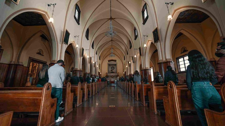 Interior de la iglesia de Monserrate, con sus arcos, vitrales, bancas de madera y visitantes en oración.