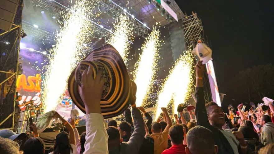 Público celebra frente a un escenario con fuegos artificiales, levantando sombreros durante un concierto nocturno.
