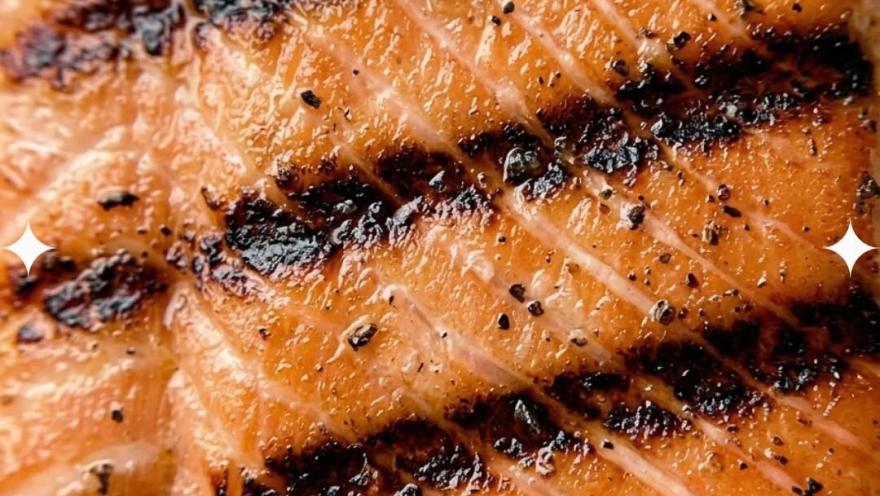 Primer plano de un filete de pescado a la parrilla, con marcas de cocción, textura jugosa y un acabado dorado y especiado.