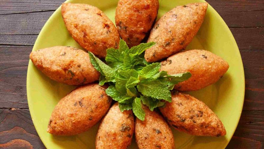  Empanadas de quinua doradas y crujientes, dispuestas en forma circular sobre un plato, acompañadas de hojas de hierbabuena.