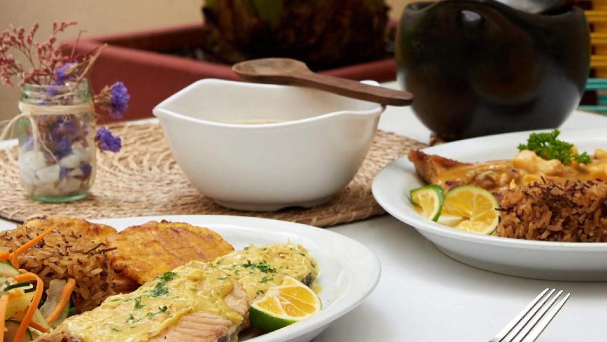 Platos de cocina colombiana con filete de pescado, arroz, patacones y ensalada, acompañados de limón y salsas.
