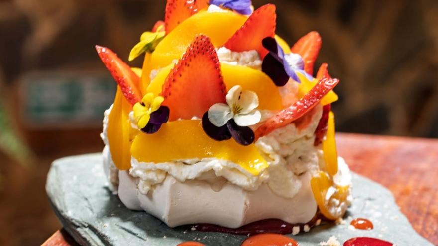Meringue and cream dessert, decorated with strawberries, peach, edible flowers, and fruit coulis, presented in an artisanal and colorful way.