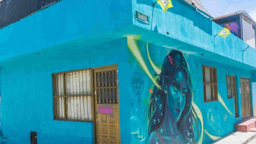 Casa de fachada azul en Ciudad Bolívar, decorada con un colorido mural de arte urbano que retrata el rostro de una mujer.
