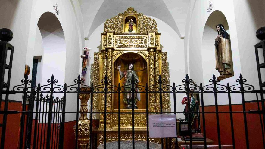 Retablo dorado con esculturas religiosas en una capilla lateral de la iglesia de San Juan de Dios, rodeado de detalles ornamentales y una reja de hierro.