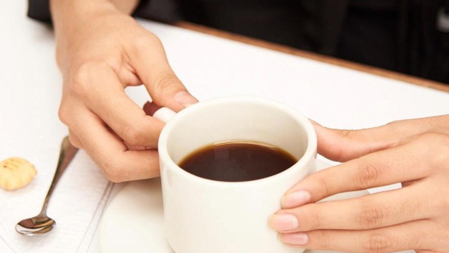 Taza de café negro servida sobre una mesa, acompañada de una galleta y dispuesta para disfrutar de una pausa.