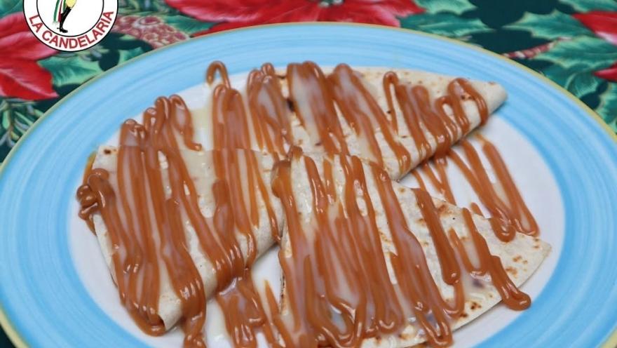 A Mexican dessert of soft tortillas smothered in a generous amount of arequipe, served on a blue plate over a floral tablecloth.