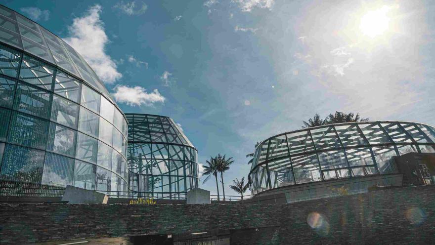 Vista del Tropicario del Jardín Botánico de Bogotá, con sus estructuras de vidrio y acero iluminadas por el sol.