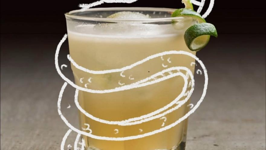 Cóctel de tono cítrico servido en vaso bajo, decorado con una rodaja de limón y un creativo dibujo de una serpiente blanca alrededor.
