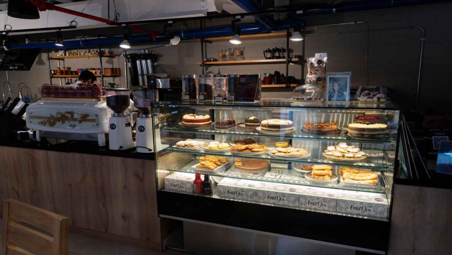 Vitrina de cristal iluminada con tortas, horneados y empanadas junto a una máquina de café expreso profesional.