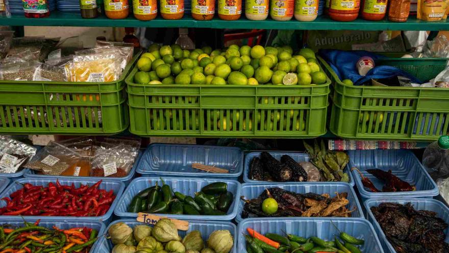 Puesto de mercado con canastas de limones, ajíes, tomatillos, especias, hierbas y salsas de diferentes variedades.