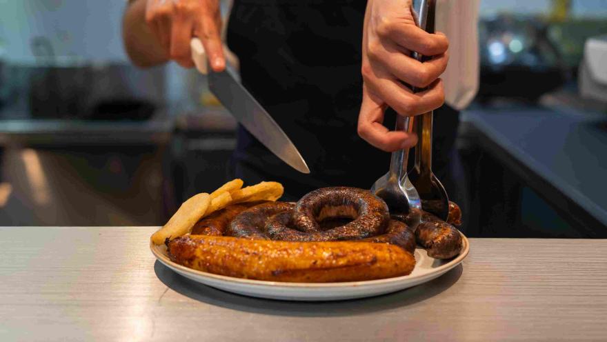 Plato con chorizos, morcilla, plátano maduro y papas, servido mientras es preparado en cocina.