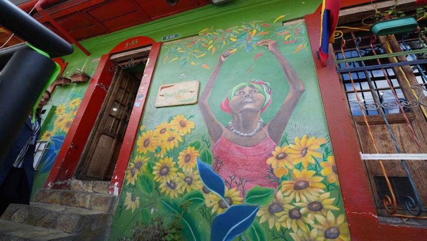 Detalle de mural en fachada verde con una mujer cosechando ajíes y el letrero de madera del restaurante. 