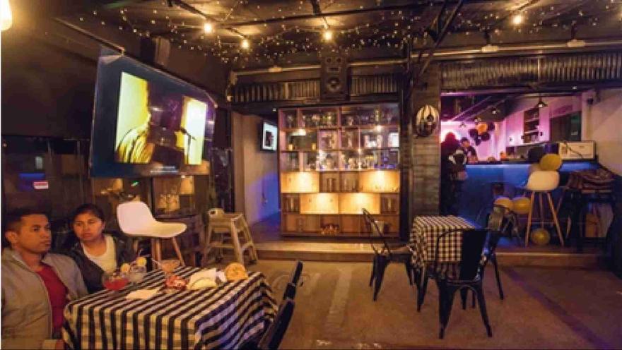 Pareja sentada en una mesa con mantel a cuadros disfrutando de bebidas en un bar con pantalla de televisión. 