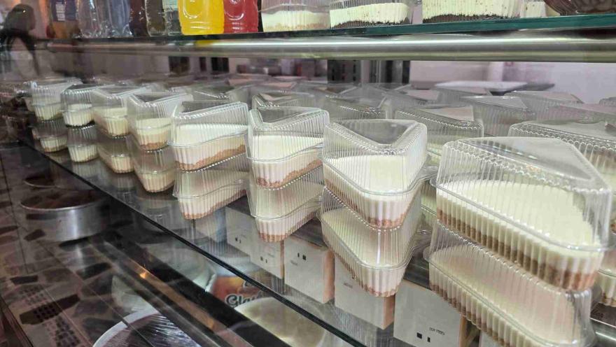 Múltiples porciones individuales de cheesecakes en envases plásticos triangulares apilados dentro de una vitrina.