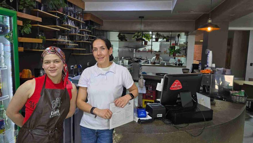 Dos colaboradoras sonríen detrás de la barra de atención del restaurante cerca del punto de pago. 