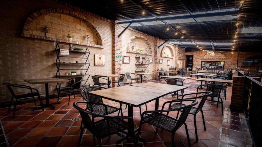 Salón de restaurante con paredes de ladrillo, arcos decorativos, suelo de terracota y mesas de madera con sillas negras.