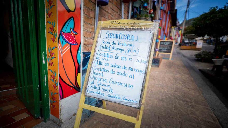 Tablero informativo de madera con el menú del día escrito a mano en la entrada del restaurante Sazón Costeño.