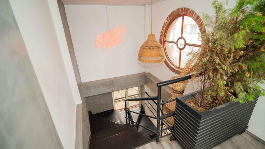 Escalera de madera oscura con barandilla metálica, lámpara tejida, maceta con vegetación y letrero luminoso de Aperol Spritz.