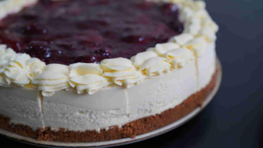  Cheesecake entero sobre base de galleta, decorado con crema chantilly y cobertura de mermelada de frutos rojos. 