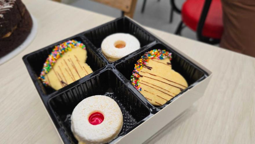 Caja organizadora negra con galletas de mantequilla en forma de corazón con chispas de colores y alfajores. 