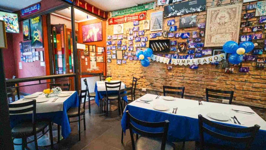 Vista en ángulo de mesas de madera vestidas de blanco y azul dispuestas junto a la pared decorada con fotografías.