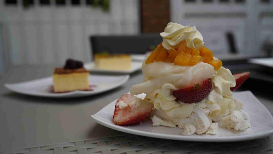 Postre de merengón con crema batida, fresas frescas y trozos de mango servido en plato blanco sobre una mesa. 