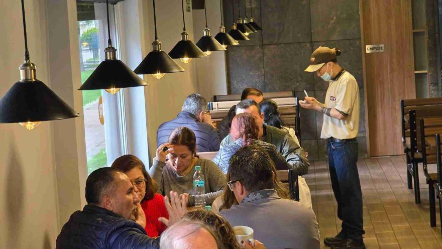 Mesero tomando un pedido a clientes sentados en el comedor iluminado por lámparas colgantes en Kuty. 