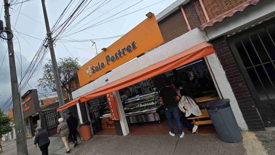 Entrada del local Solo Postres con toldo naranja, personas conversando en mesas de madera y peatones transitando.