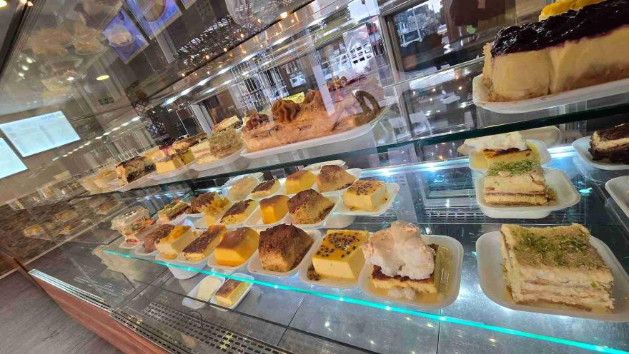 Vista panorámica de mostrador refrigerado con repisas llenas de tortas, flanes y postres individuales. 