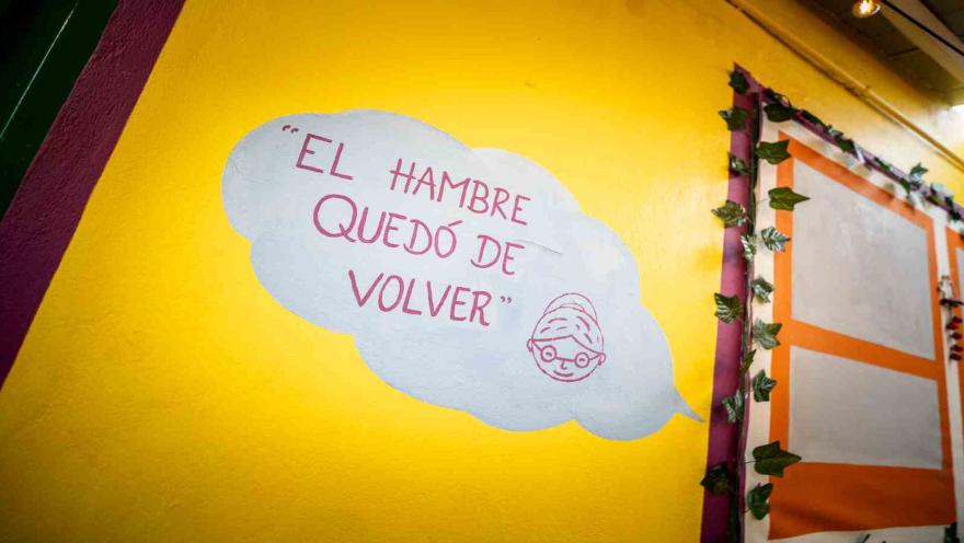 Pared amarilla decorada con la frase El hambre quedó de volver pintada dentro de una nube de pensamiento.