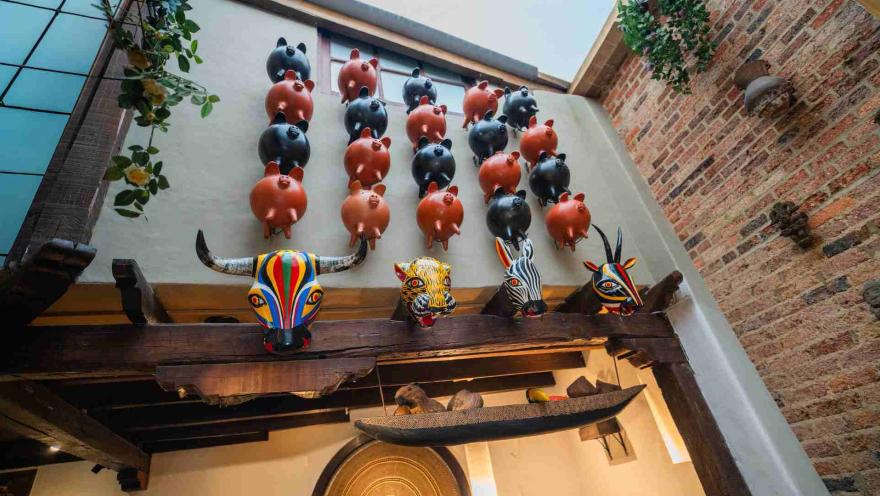  Alcancías de cerditos de arcilla en la pared superior y máscaras tradicionales de madera del Carnaval de Barranquilla.