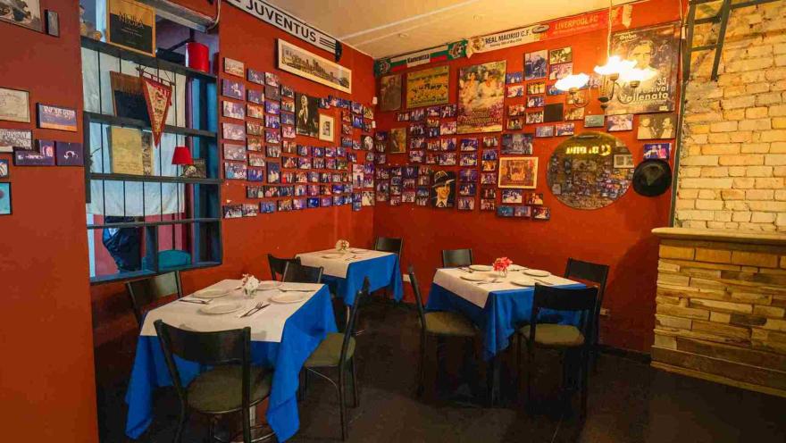  Esquina del restaurante con paredes de tono rojo intenso repleta de cuadros, fotos memorables y un espejo circular decorativo.