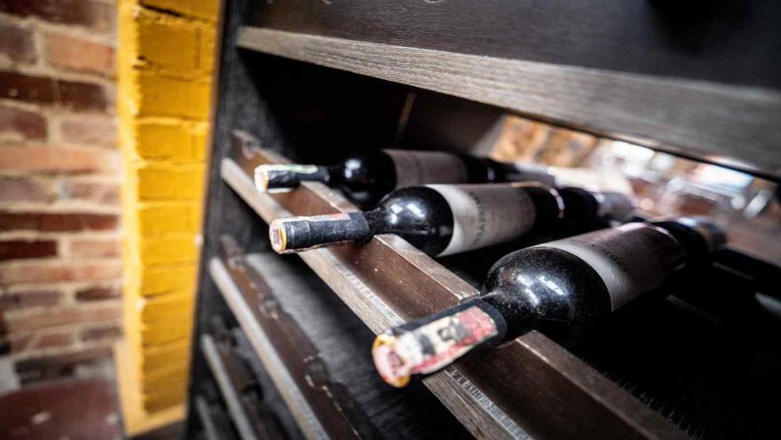 Primer plano en ángulo de botellas de vino tinto acostadas en compartimentos de un botellero de madera oscura.