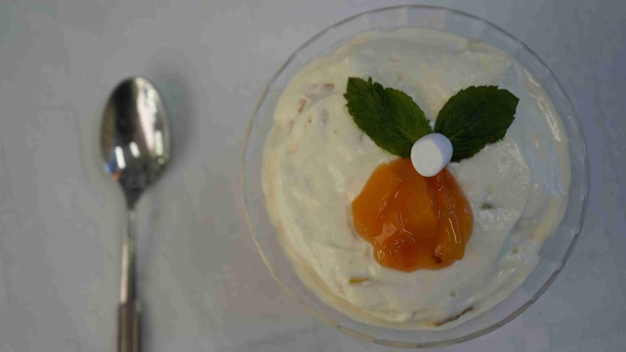 Copa de vidrio con crema, melocotón, malvavisco y hojas de menta vista desde arriba.