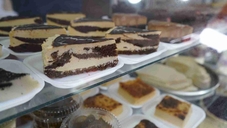 Porción de pastel de tres capas de chocolate y crema exhibido en primer plano dentro de una vitrina refrigerada. 